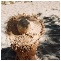 Jonge vrouw met een zonnehoed, ontspannen in de schaduw op het strand, die de zonbeschermende eigenschappen van Dermasence Solvinea benadrukt.